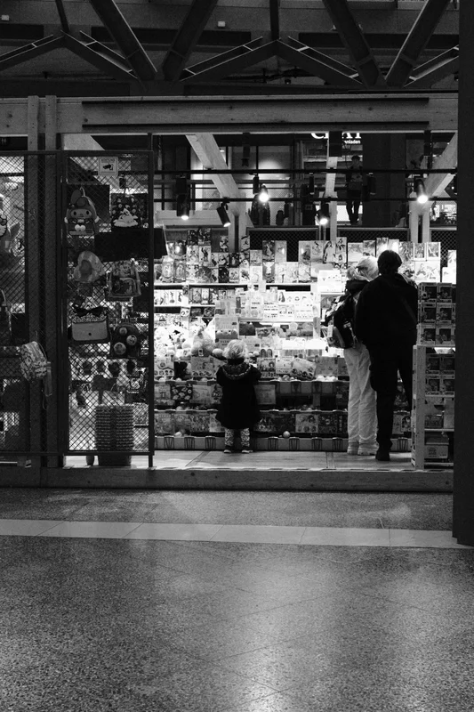 People stand in front of a storefront display filled with posters and small items under a roof.