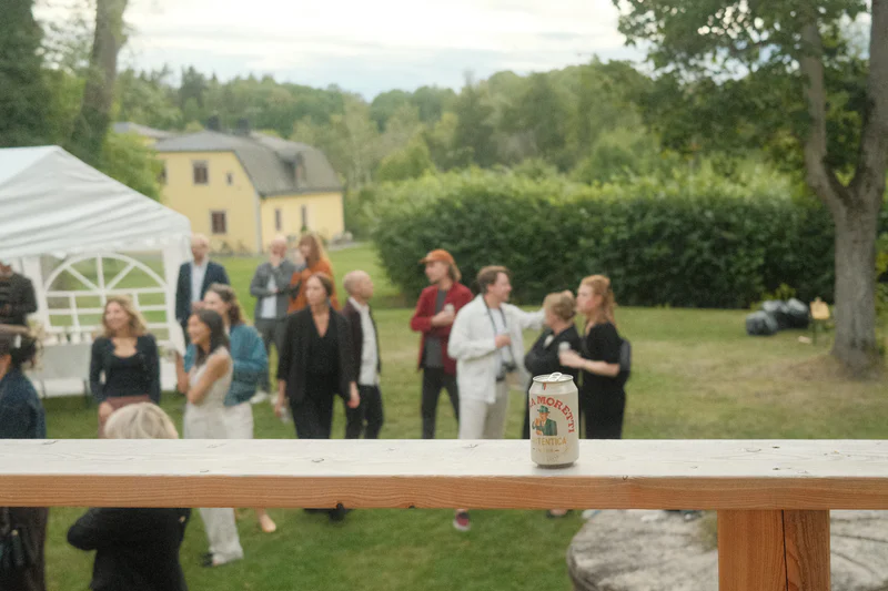 Beer can on a wooden railing with people and tents in the background.