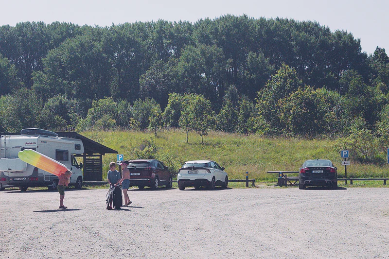 Kids walk on a gravel parking lot near vans and cars with trees in the background.