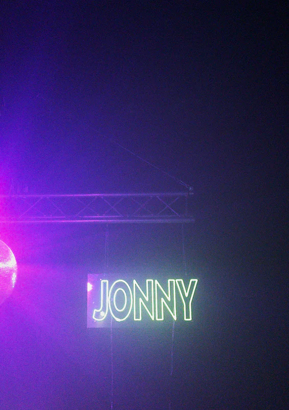 Purple stage light with the word “JONNY” glowing in white against a dark backdrop.
