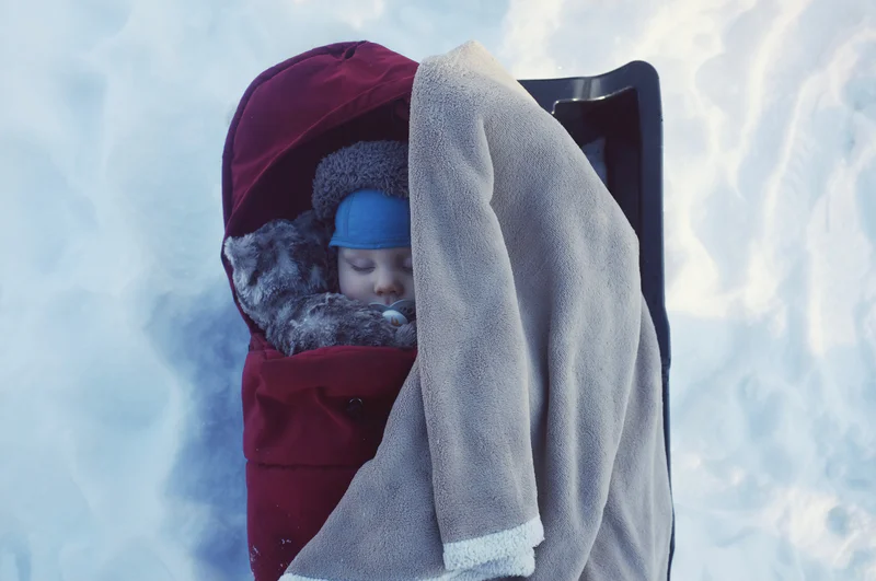 Child in a purple winter hat and red jacket peeks from inside a stroller with a blanket.