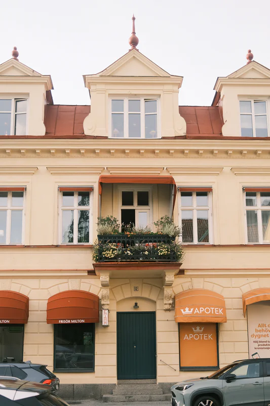 Facade of a cream building with storefronts and flower boxes, including an apotek sign above the entrance.