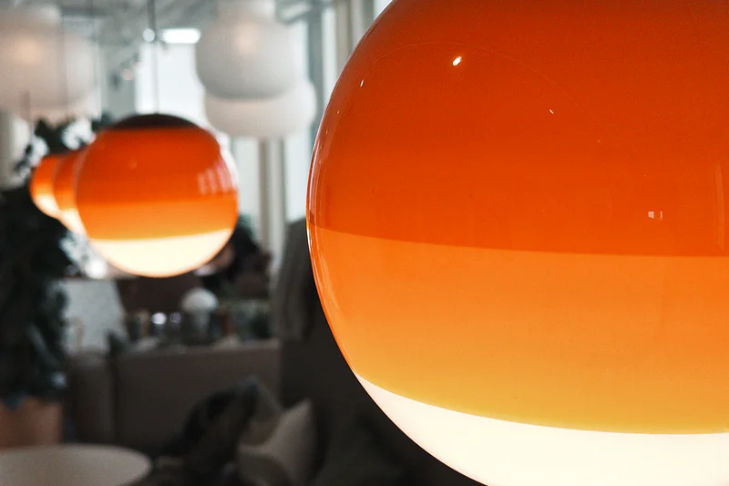 Close-up of two glowing orange glass pendant lamps indoors, with one large lamp in the foreground.